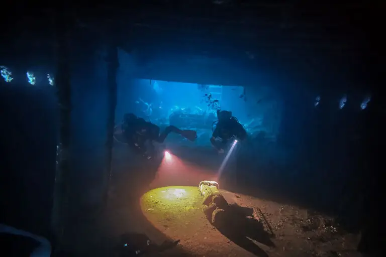 Gerätetaucher mit Taschenlampen erkunden innere Abteilung des USAT Liberty Schiffswracks während Nachttauchgang in Tulamben