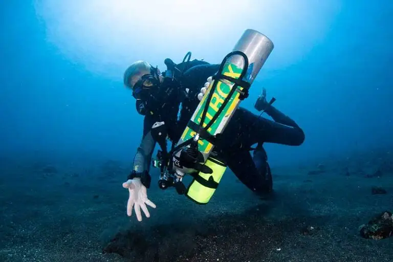 Gerätetaucher mit Nitrox-Flasche taucht über vulkanischem Sandboden in Tulamben, Bali Gewässern