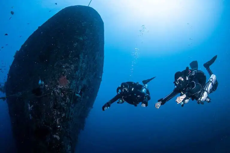Zwei Taucher erkunden das Heck des USAT Liberty Schiffswracks in Tulamben, Bali vor blauem Wasserhintergrund