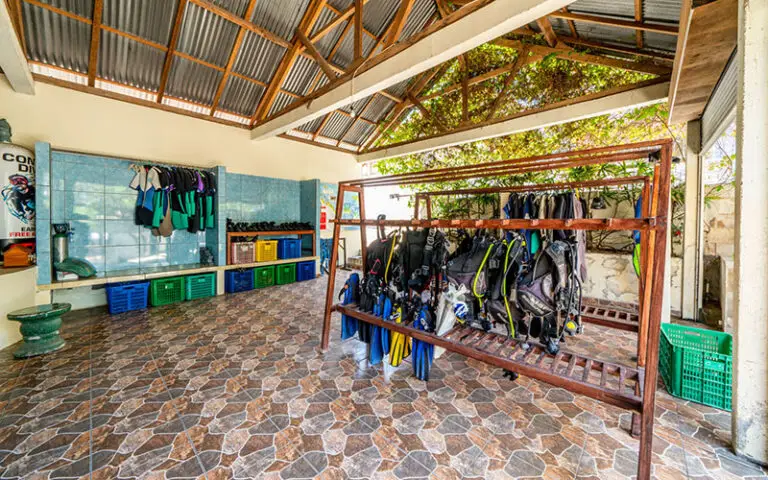 Salle d'équipement du centre de plongée Ocean Sun avec matériel de plongée, combinaisons et palmes organisés sur des supports à Tulamben, Bali