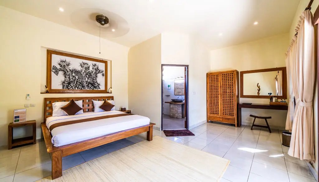 Spacious bungalow bedroom at Ocean Sun Dive Resort with wooden furniture and traditional Balinese decor in Tulamben