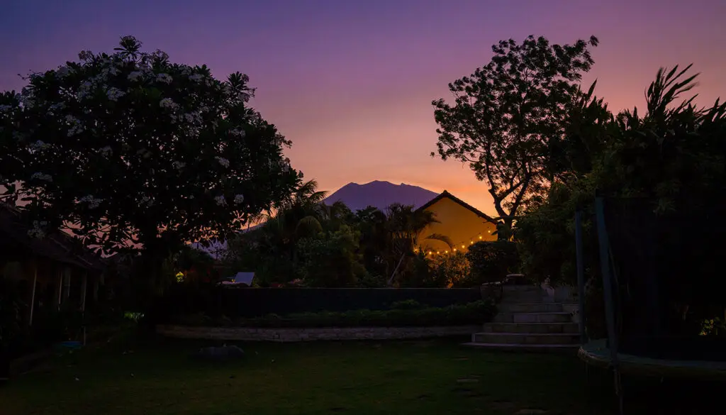 Ocean Sun Dive Resort at sunset with Mount Agung silhouette, tropical gardens, and purple-orange sky in Tulamben, Bali